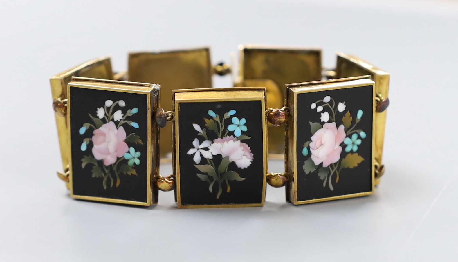 A 19th century Florentine yellow metal bracelet, set with seven pietra dura panels, decorated with flowers, 17cm, gross weight 36 grams.